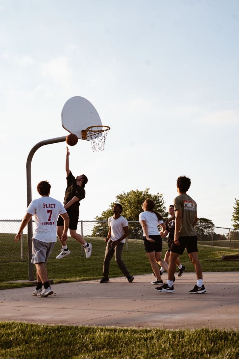 Partie de basket improvisée sur un terrain de quartier à l'heure dorée, groupe mixte d'amis