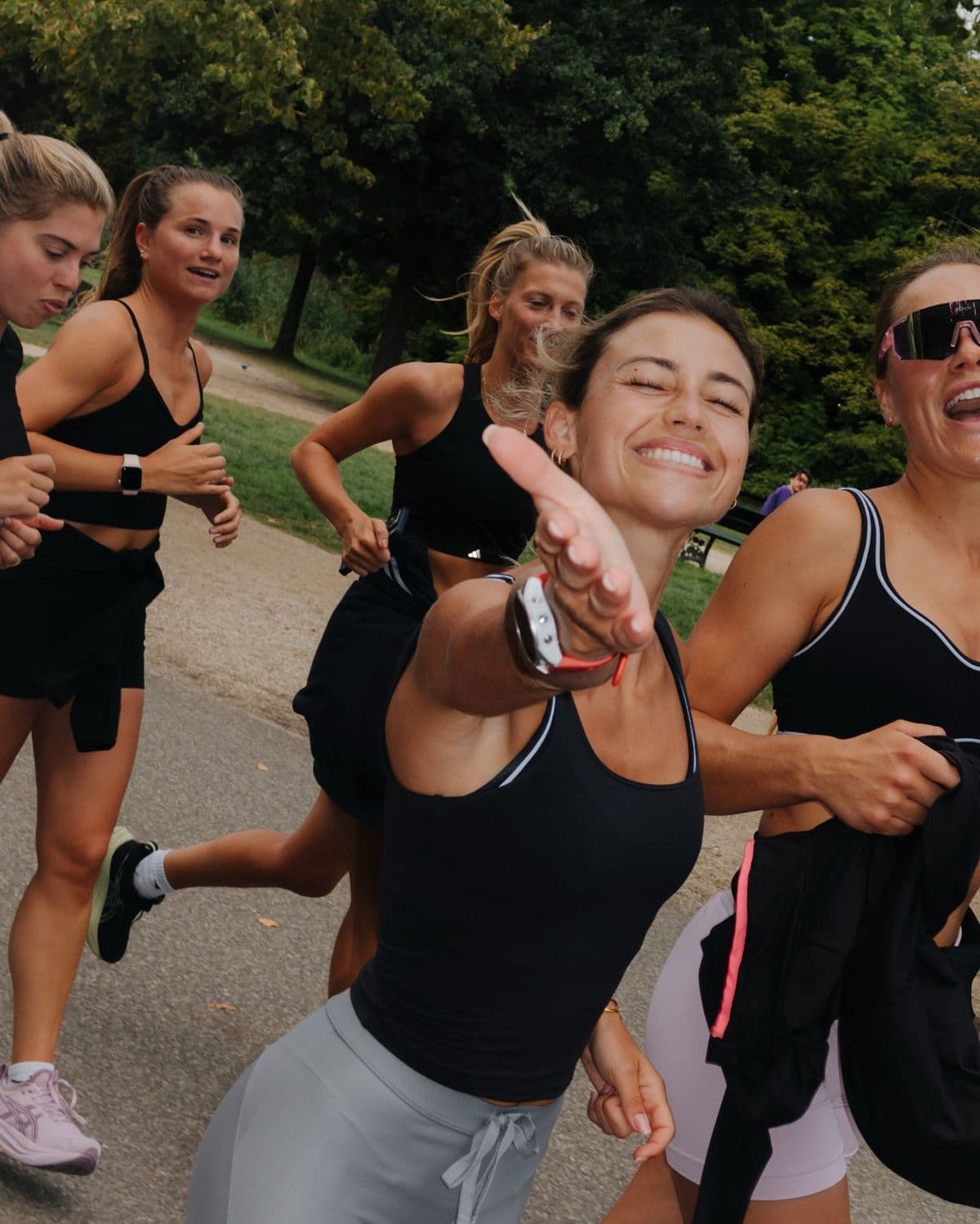 Groupe de coureuses souriantes dans un parc, une main tendue vers l'objectif, ambiance complice