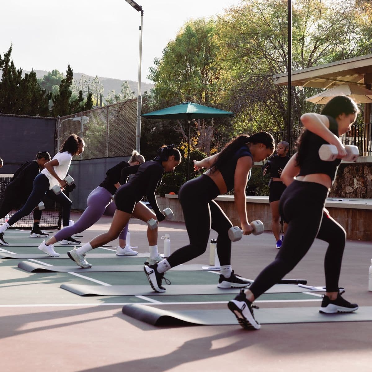 Classe de fitness en plein air en fin de journée, ligne de participants enchaînant un mouvement avec haltères