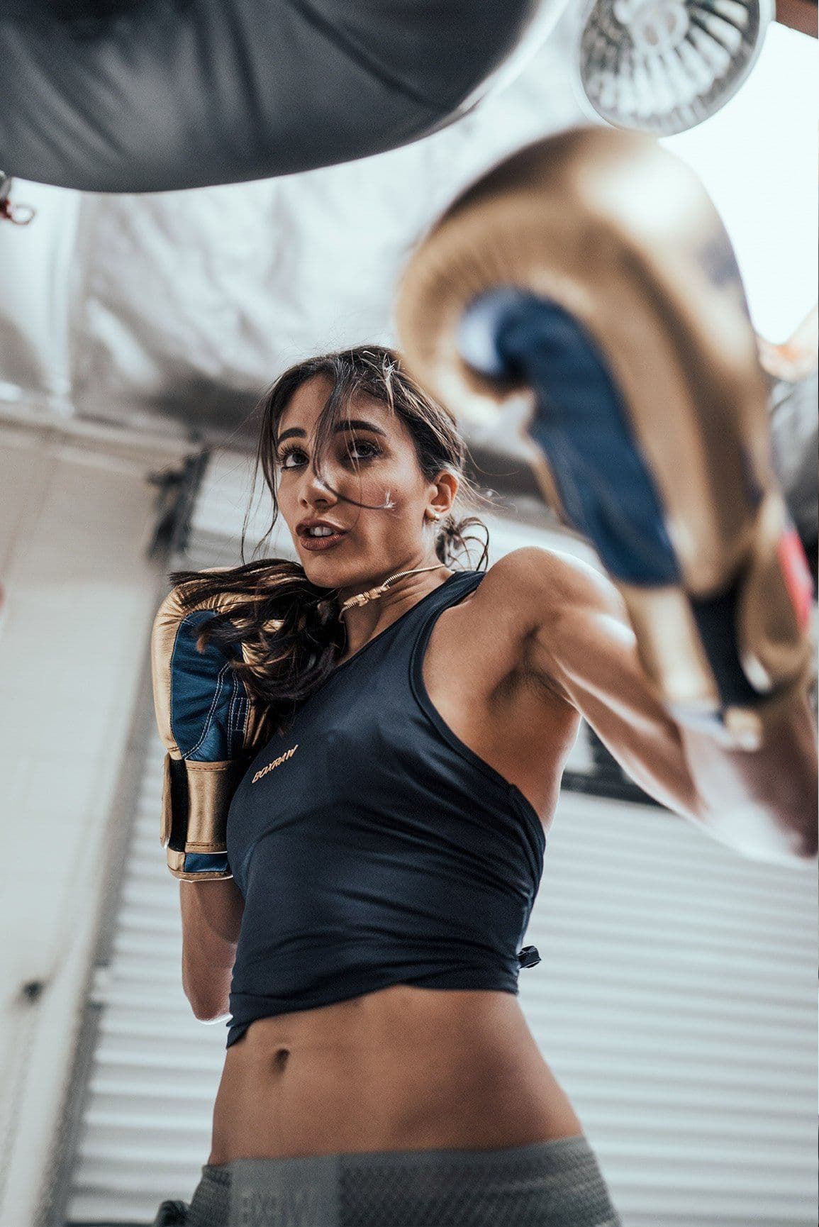 Athlète à l'entraînement de boxe, gants dorés, sac de frappe en arrière-plan, éclairage cinéma