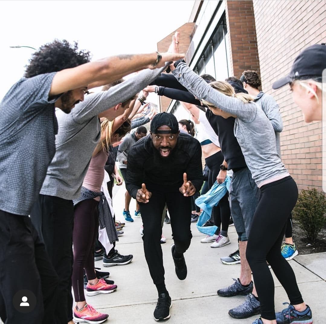 Coureur traversant une haie d'honneur formée par les membres d'un running club, façade en brique urbaine